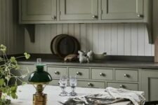 a vintage green kitchen with grey soapstone countertops, a white stone table, a white beadboard backsplash is amazing