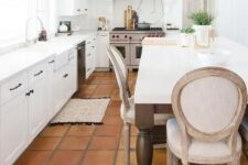 a vintage-inspired white kitchen with only lower cabients, a large cooker and a hood, stained beams, a large table that is a kitchen island