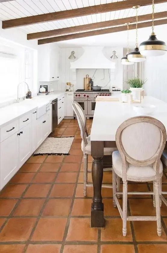a vintage inspired white kitchen with only lower cabients, a large cooker and a hood, stained beams, a large table that is a kitchen island
