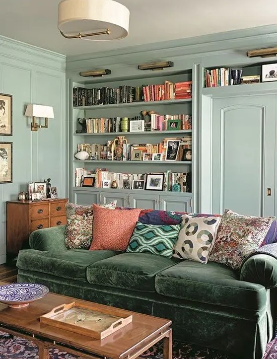 a vintage mint green living room with built-in bookshelves, a green sofa and bright pillows, a stained table and a sideboard