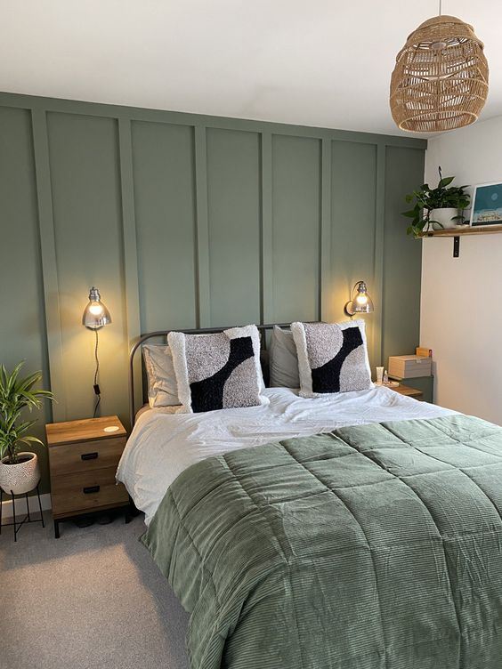 a welcoming bedroom with a sage green paneled wall, a metal bed with sage and white bedding, stained nightstands and a woven pendant lamp