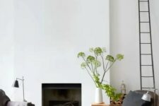 a welcoming living room with a minimalist fireplace, a couple of chairs, greenery, a ladder and a black lamp
