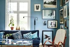 a welcoming living room with dusty blue walls, a creative gallery wall, a navy sofa, a glass coffee table and a rocker chair