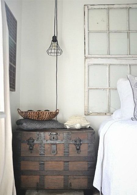 a white Scandi bedroom with a stained trunk as a nightstand and storage unit, a bed, window frames and a black pendant lamp