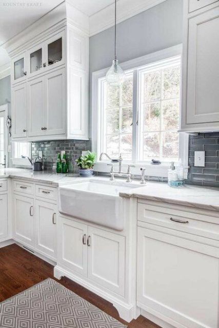 a white farmhouse kitchen with a grey tile backsplash, white countertops, casement windows and pendant lamps