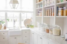 a white farmhouse kitchen with open and shaker style cabinets, white stone countertops and a white lantern hanging