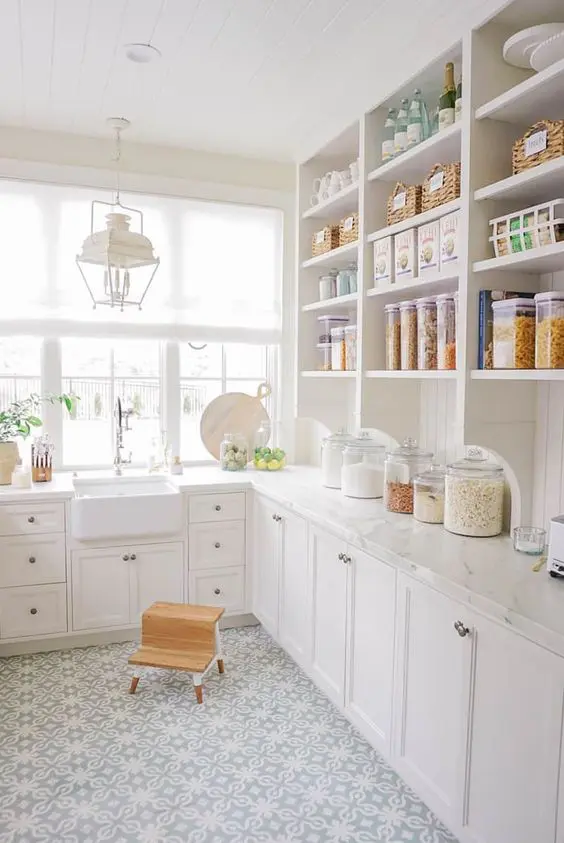 a white farmhouse kitchen with open and shaker style cabinets, white stone countertops and a white lantern hanging