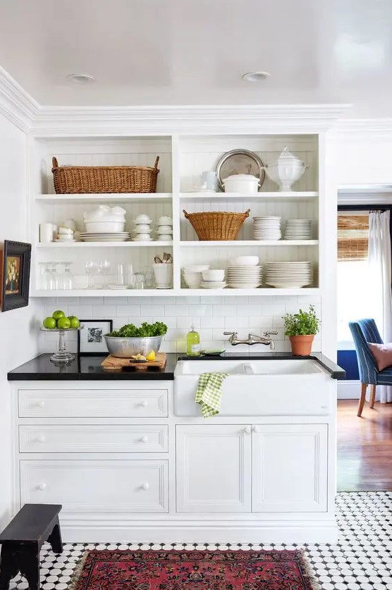 a white farmhouse kitchen with shaker and open cabinets, black countertops and potted plants and beautiful decor