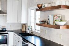 a white farmhouse kitchen with shaker cabinets, black soapstone countertops, a neutral tile backsplash and open shelving