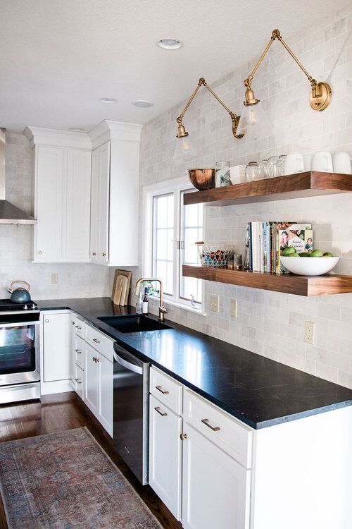 a white farmhouse kitchen with shaker cabinets, black soapstone countertops, a neutral tile backsplash and open shelving