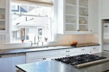 a white farmhouse kitchen with shaker cabinets, black soapstone countertops, a window as a backsplash