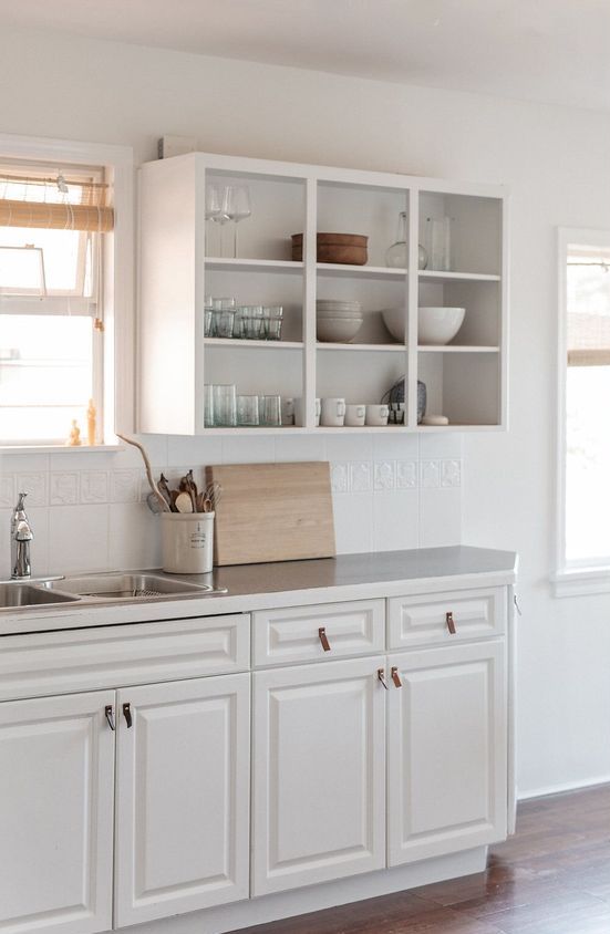 a white kitchen with open and shaker cabinets, neutral countertops and large scale tiles on the backsplash