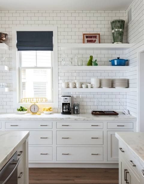 a white kitchen with shaker and flat panel cabinets, white open shelving, white subway tiles and a large kitchen island