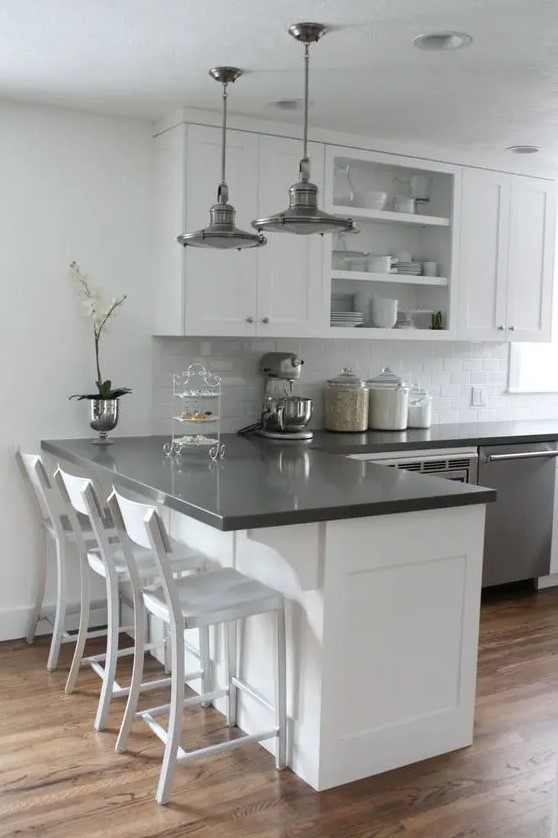 a white kitchen with shaker and open cabinets, black countertops, metal pendant lamps and a potted flower is cool and chic