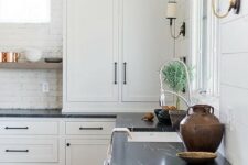 a white kitchen with shaker style cabinets, a brick backsplash, black soapstone countertops, black fixtures