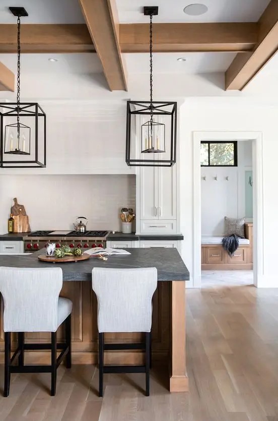 a white shaker style kitchen with a stained kitchen island, black soapstone countertops, framed hanging lamps over the island