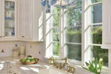 a white vintage kitchen with shaker cabinets, stone countertops, casement windows and printed curtains