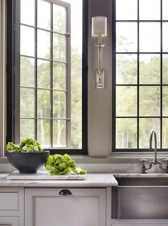an English country kitchen with a white stone countertop, chic French style casement windows and elegant lamps