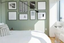 an airy Scandinavian bedroom with sage green walls, a bed with neutral bedding, a black and white gallery wall