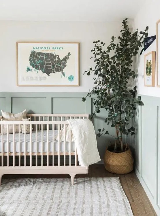 an airy and beautiful Scandinavian nursery with sage green paneling, a stained crub, neutral textiles, a potted plant and some art