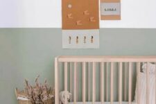 an airy and chic Scandinavian nursery with a color block sage green wall, a wooden crib, neutral bedding, a woven basket and a color block vase