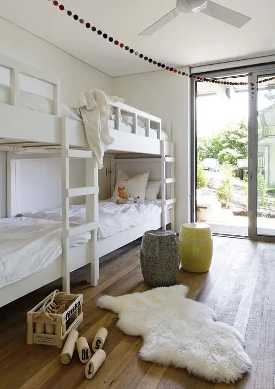 an airy kids' bedroom with built-in bunk beds with white bedding, a yellow and a grey side table and a faux fur rug