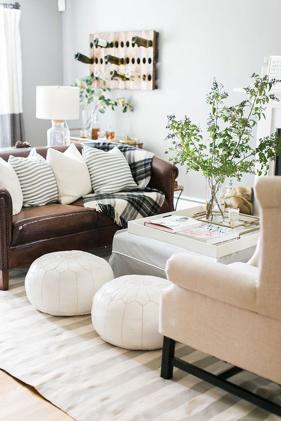 an airy living room with a brown leather and creamy sofa, white Moroccan poufs, a coffee table and greenery