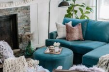 an eclectic living room with a fireplace clad with faux stone, a turquoise sofa and an ottoman, a stool, leather chairs, a chandelier