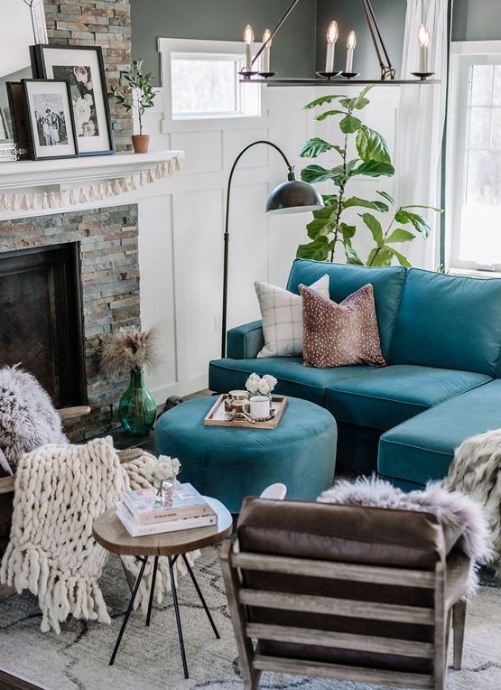 an eclectic living room with a fireplace clad with faux stone, a turquoise sofa and an ottoman, a stool, leather chairs, a chandelier