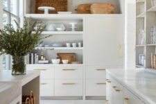 an elegant creamy kitchen with flat panel and open cabinets, baskets and wooden cutting boards, brass handles