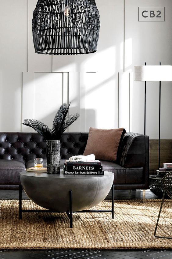 an elegant living room with a black leather sofa, a unique bowl coffee table, a blakc woven lamp and a black metal chair