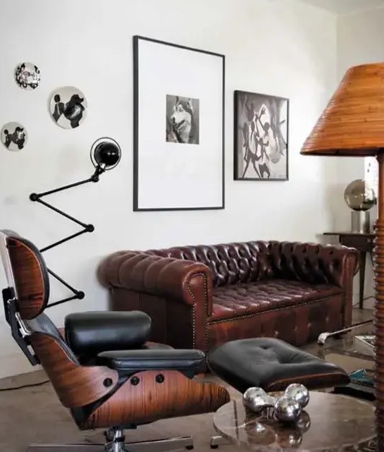an elegant living room with a brown Chesterfield sofa, a black chair with a footrest, a side table, a black and white gallery wall