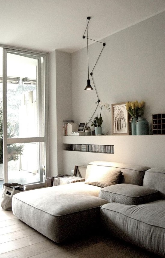 an ethereal Scandi living room with a low grey sectional, built in shelves, a black pendant lamp and some books