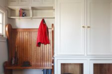 an off-white modern mudroom with shaker cabinets and a built-in dog crate in one of the lower cabinets
