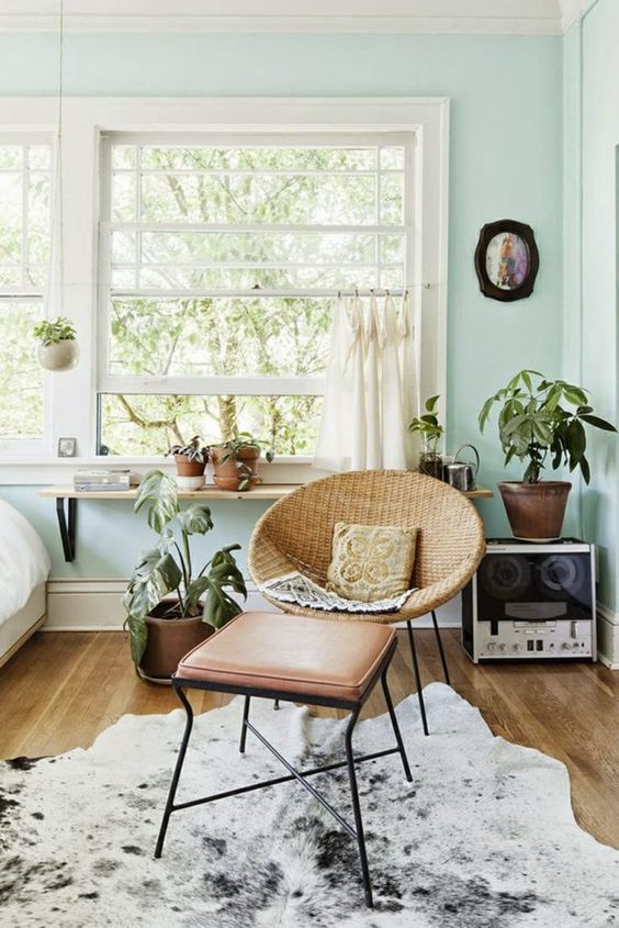 mint blue bedroom wiht a woven chair and a leather footrest, potted plants, a bed and a windowsill shelf plus a rug