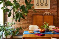 03 a mid-century modern meets boho dining room with a brick accent wall, a stained table and chairs, a rattan storage unit, potted plants and a chandelier