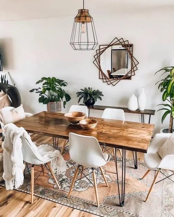 a boho dining room with a hairpin leg dining table, white chairs, a hairpin console table, potted greenery, a mirror with a catchy frame