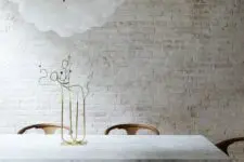 05 a refined modern dining room with a whitewashed brick wall, a marble table, modern chairs and a cluster of bulbs
