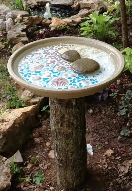 a tree stump holding a beautiful mosaic bird bath with seashells and pebbles is a lovely idea for any garden