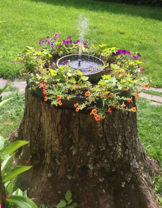a tree stump with bright blooms and a small fountain on top is a catchy and fun idea for your garden, you can DIY it