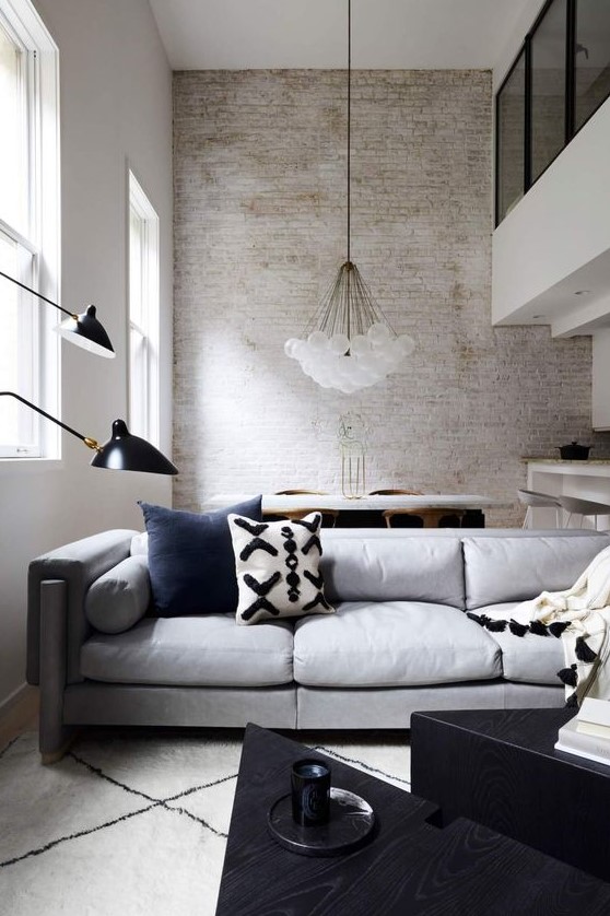a contemporary living room with a whitewashed brick wall, chic furniture, a cluster chandelier and black for a touch of drama