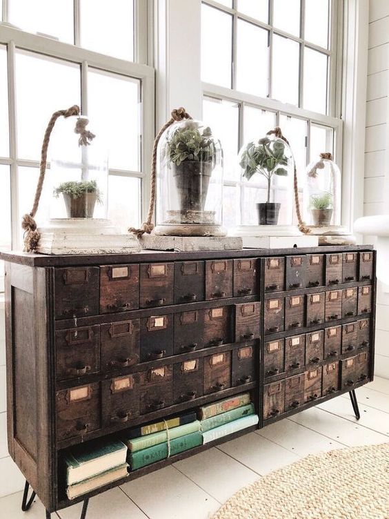 a vintage dark-stained apothecary cabinet placed on hairpin legs, with cloches with greenery and books is a beautiful idea for a vintage space