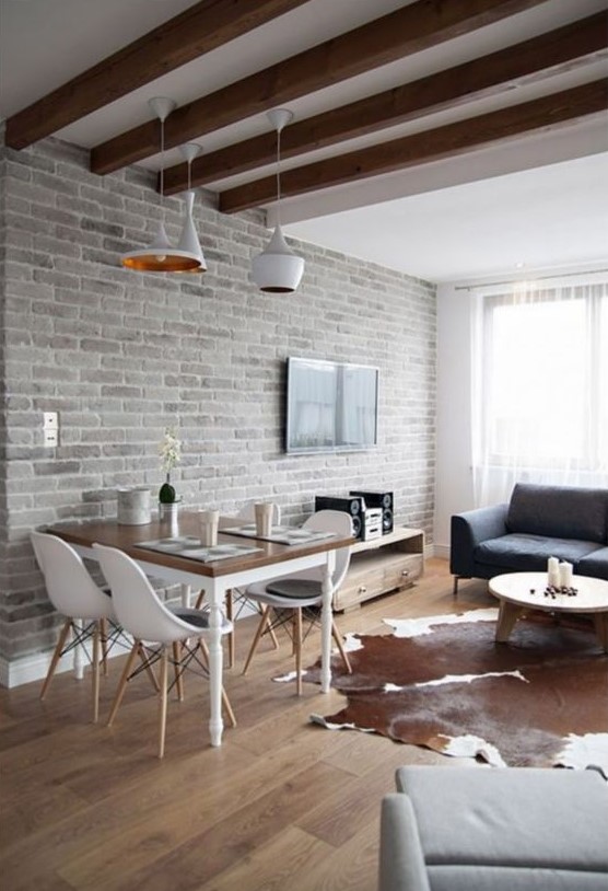 a contemporary space with a living room and a dining zone, a whitewashed brick wall, wooden beams and chic furniture