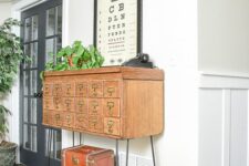 17 a vintage light-stained apothecary cabinet placed on tall hairpin legs, with suitcases under it, is a beautiful decoration for an entryway
