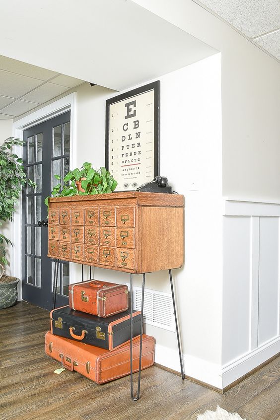 a vintage light-stained apothecary cabinet placed on tall hairpin legs, with suitcases under it, is a beautiful decoration for an entryway