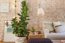 19 a living room with a whitewashed brick wall, a neutral sofa and grey poufs, side and coffee tables, potted plants and lamps