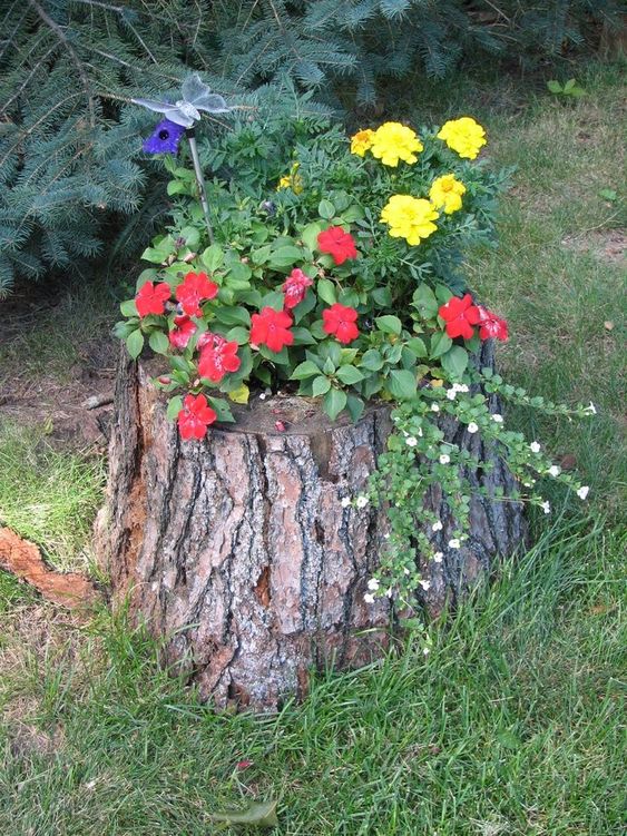 a tree stump with bold blooms and greenery and a butterfly on top is a stylish and catchy idea for a garden