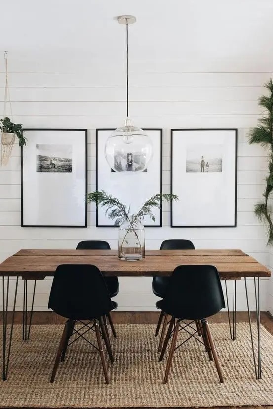 a Scandinavian dining room with a hairpin leg dining table, stylish black chairs, a gallery wall and some greenery around