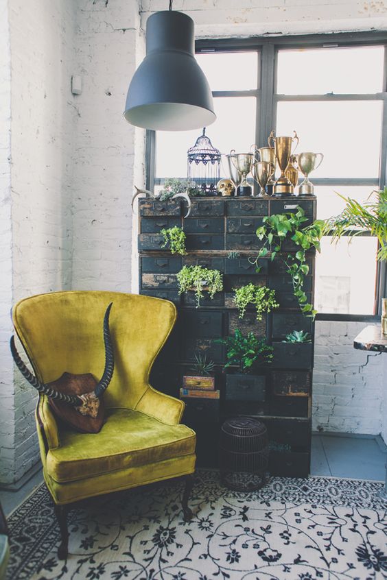 a black shabby chic card cabinet as a storage unit and a plant stand, a mustard wingback chair and a pendant lamp create a chic vintage nook