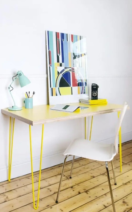 a sleek and delicate lightweight desk with neon yellow hairpin legs, a bold artwork, a blue table lamp and white chair